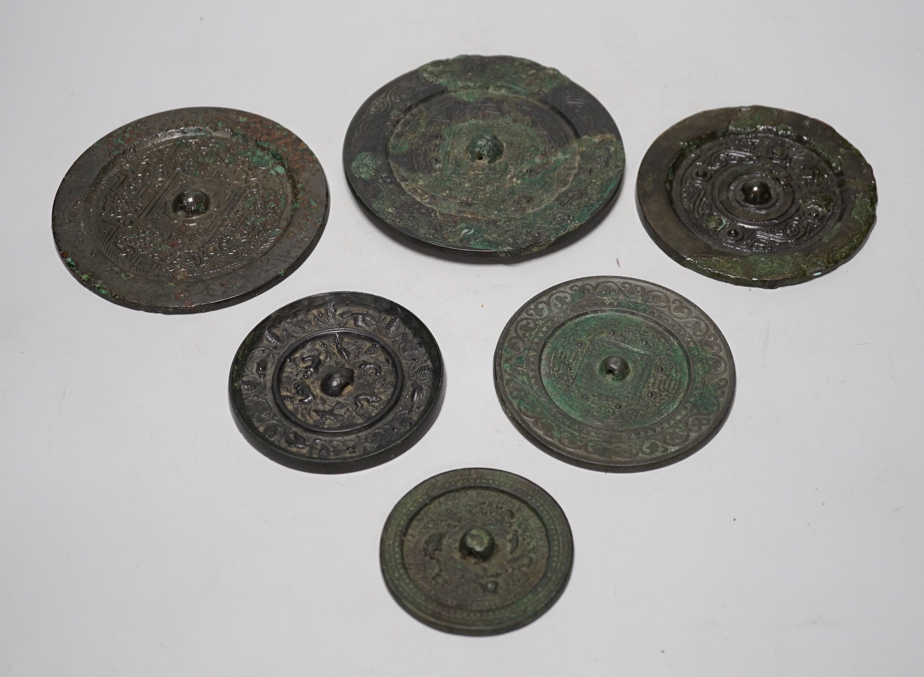A group of six Chinese archaic bronze mirrors, including two Han dynasty TLV mirrors, and a Tang dynasty squirrel and vine small mirror, five corroded, largest 14cm diameter
